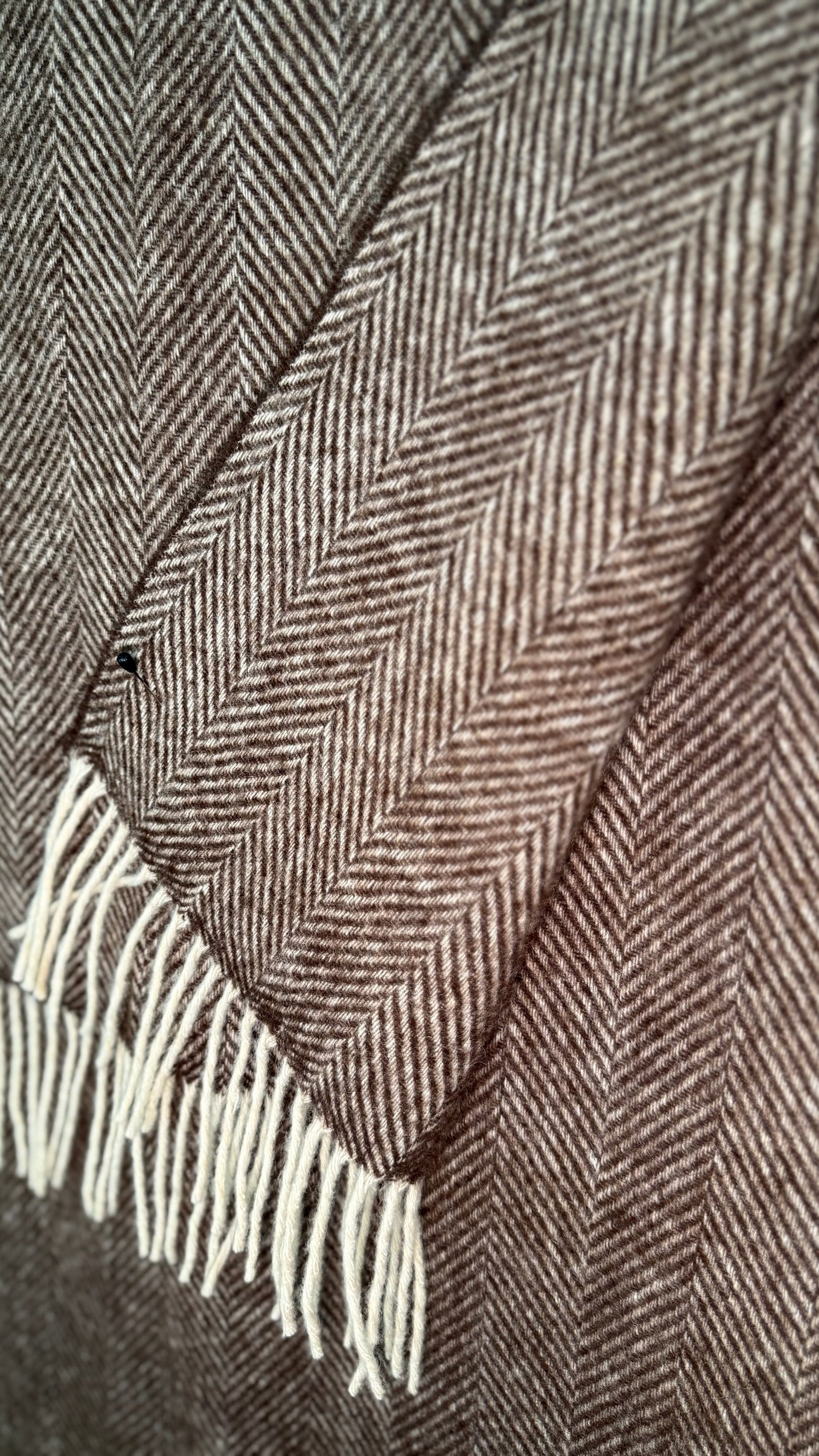 Close-up of a brown and beige herringbone patterned fabric with white fringe.