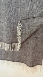 Gray herringbone blanket with white fringe on a light gray background